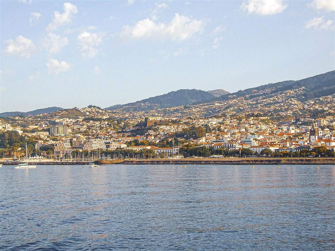 Funchal cityscape rising up hillsides from the harbor, seen across the bay from offshore