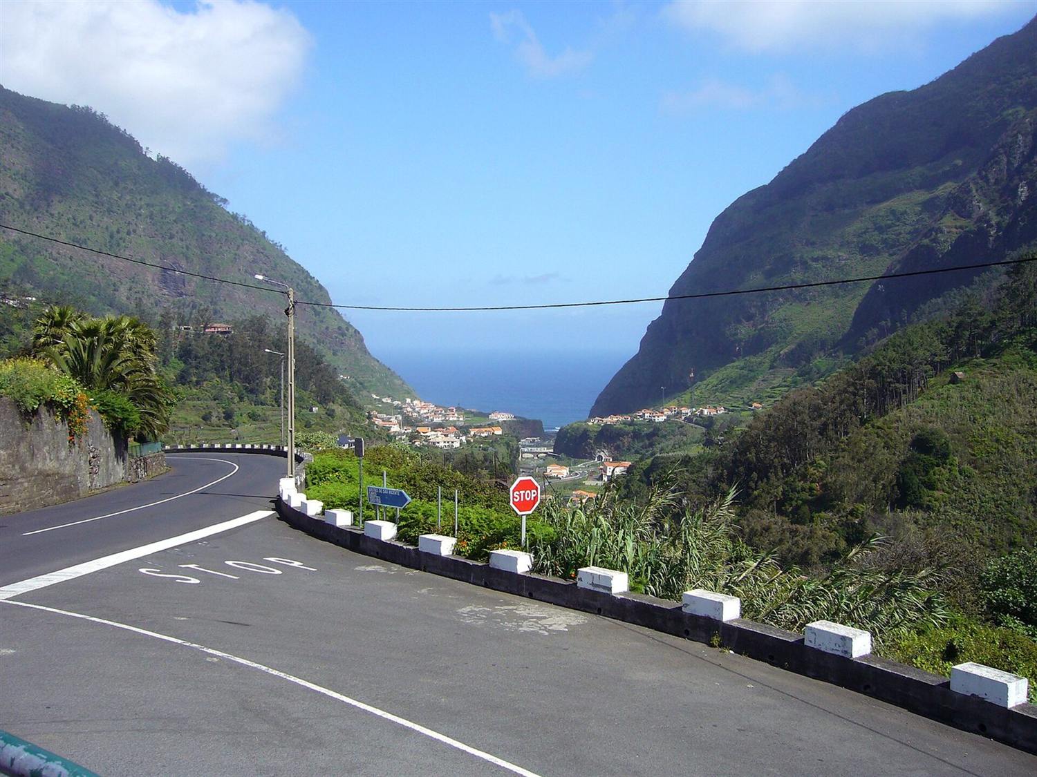 Winding mountain road with STOP sign descending toward São Vicente valley and the Atlantic coast, Madeira