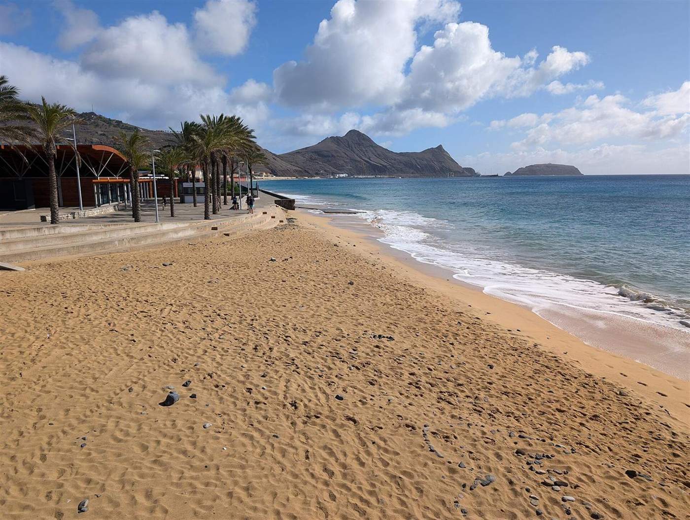 Golden sand beach with palm-lined promenade at Cais Velho, Porto Santo, mountains across the bay