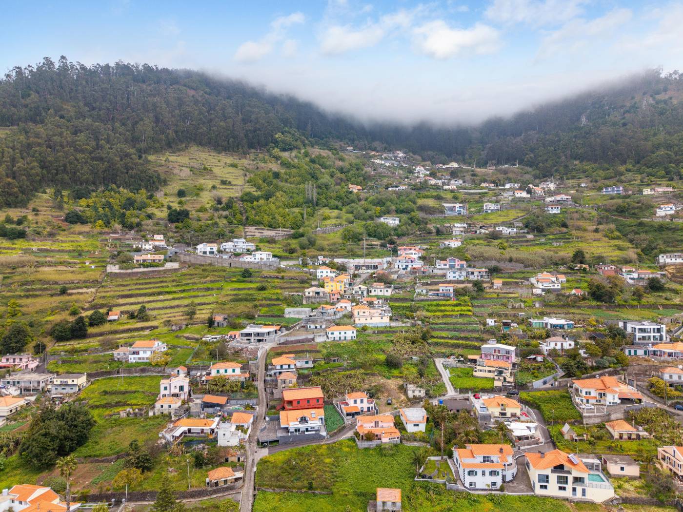 Wide aerial view of the valley and village below the plot, with low cloud over the surrounding hills