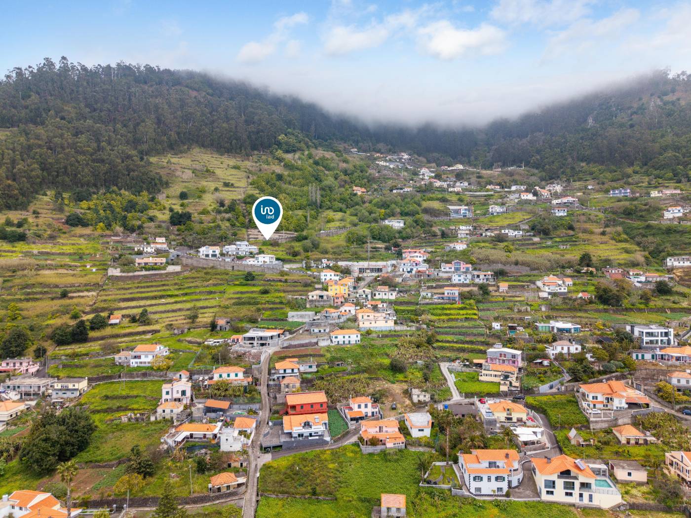 Wide aerial view of the valley and village below the plot, marked by the listing agency's location pin