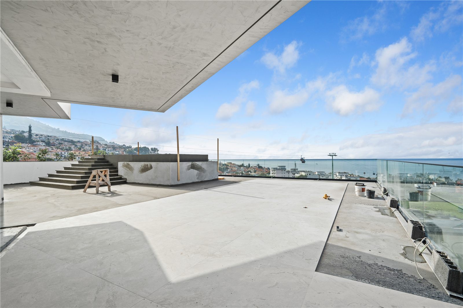 Upper terrace in bare concrete with a glass balustrade and an open sea horizon