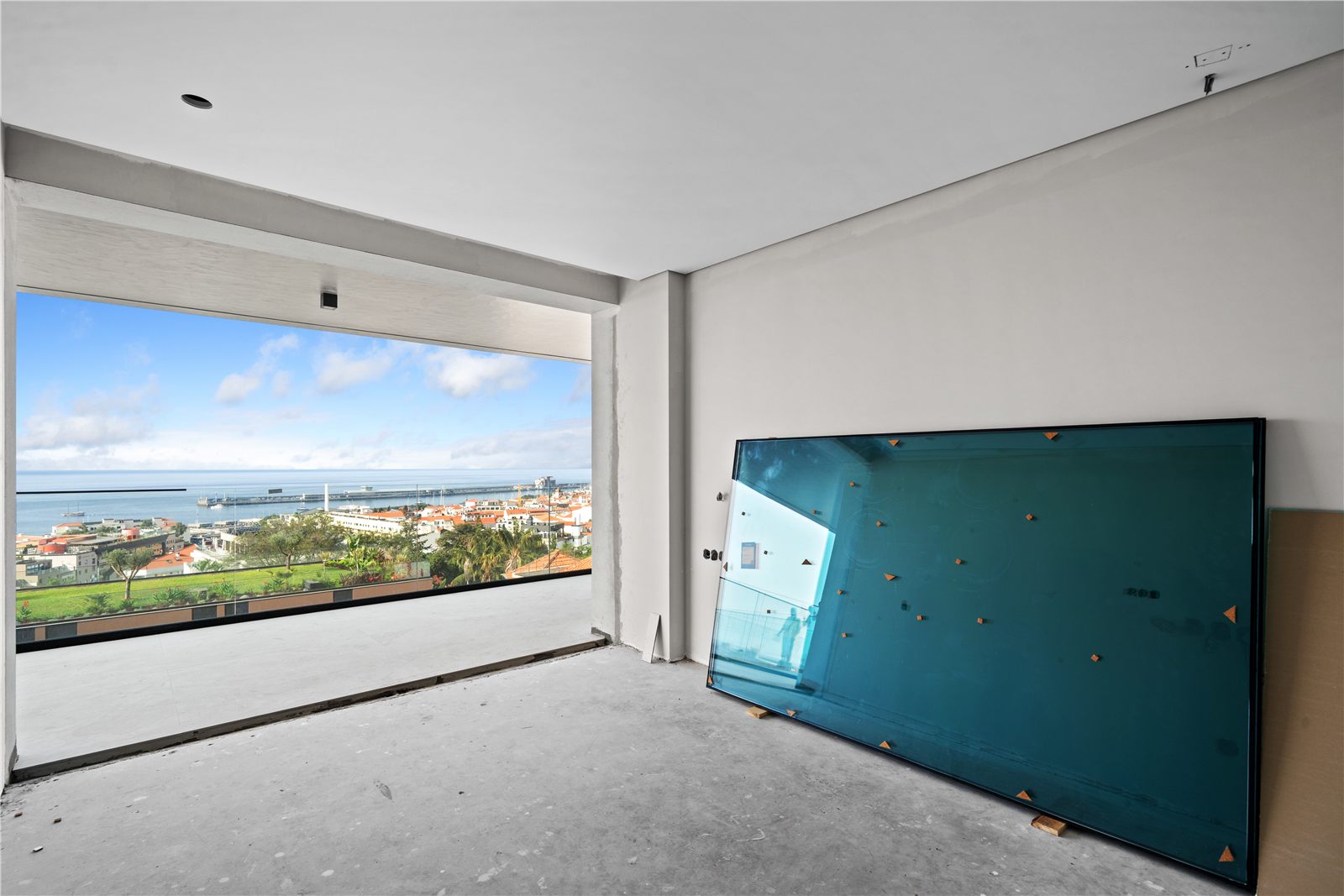 A room with a full-width window over Funchal and a large glazing panel leaning against the wall
