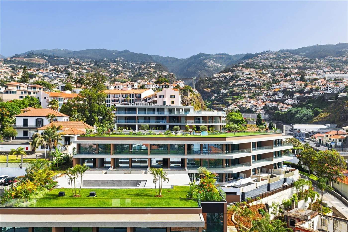Aerial view of the Uptown Lux blocks with lawns and the communal pool, Funchal houses on the slope behind
