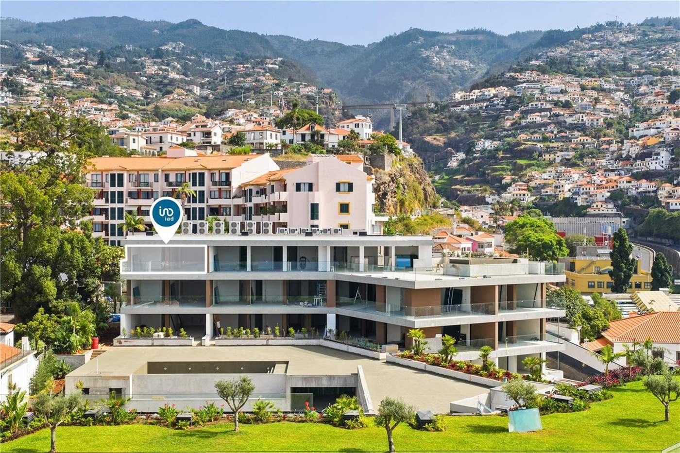 Aerial view of the Uptown Lux development, white balconied blocks stepping down a green slope with Funchal houses above