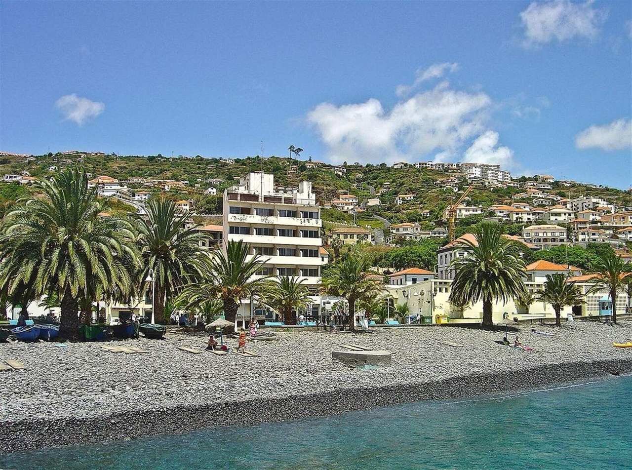 The pebble beach and palm-lined seafront at Santa Cruz, Madeira, with fishing boats drawn up on the shore and the town rising on the hillside behind