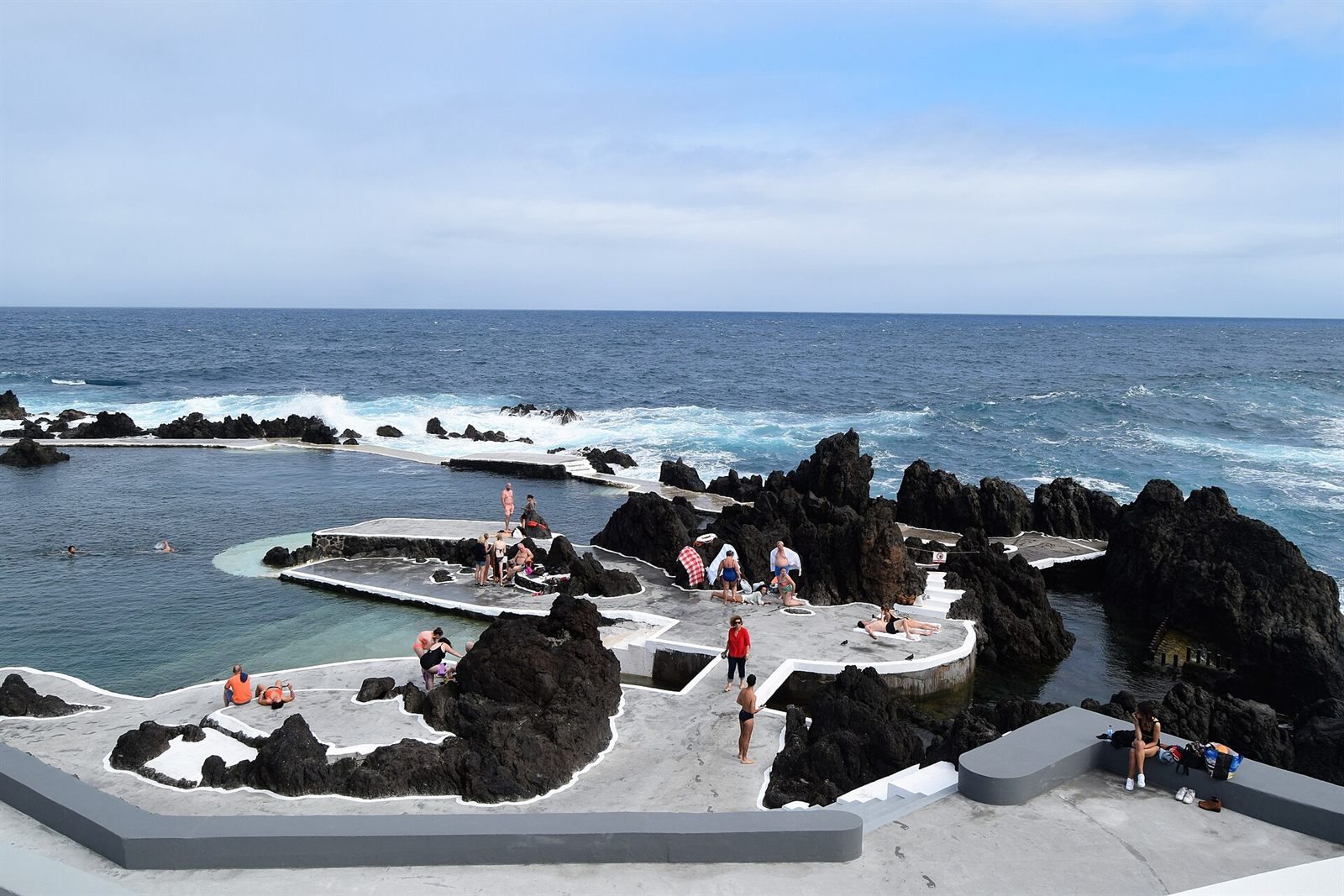 Natural volcanic rock pools at Porto Moniz, Madeira, with people sunbathing and swimming by the sea