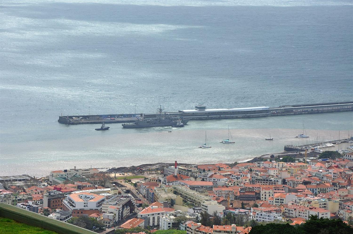 Aerial view of Funchal harbor, Madeira, with a naval ship docked and orange-roofed city below