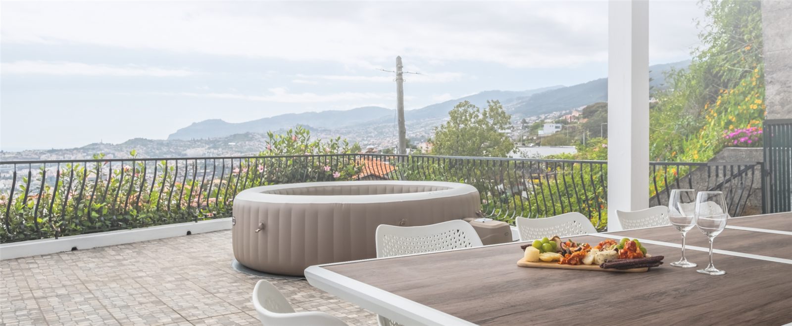 Covered terrace with an inflatable jacuzzi and a laid table, looking out over Funchal and the hills
