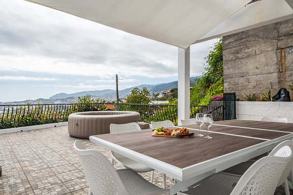 Dining table on the terrace under the canopy with the coastline behind