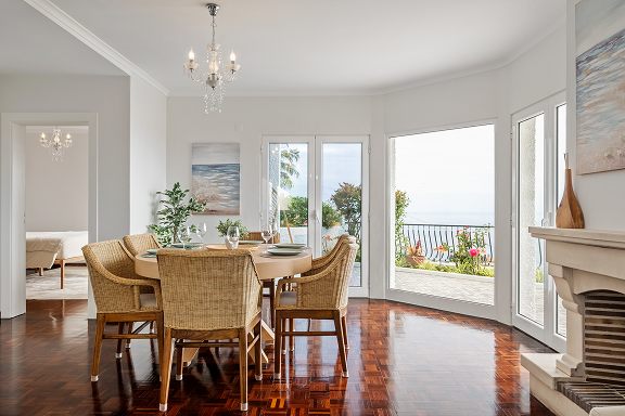 Living and dining room with tall windows facing the sea