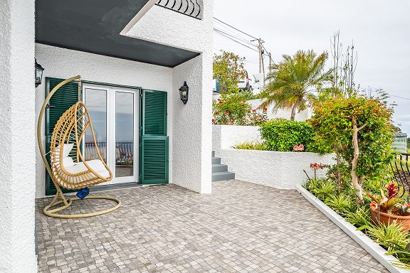 The front of the house, a hanging rattan chair beside green shutters and a planted courtyard