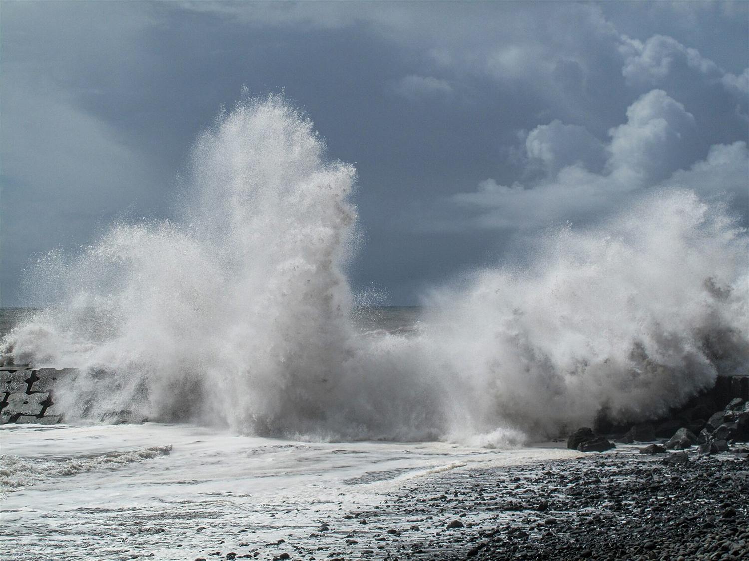 Massive wave exploding over a rocky breakwater against a stormy sky in Madeira, Portugal